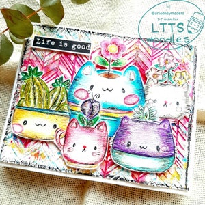 May include: A white card with a pink and white chevron pattern. The card has a black border and the text "Life is good" in black. There are five cartoon cats in flower pots, each with a different color and design. The cats are all smiling and have big eyes.