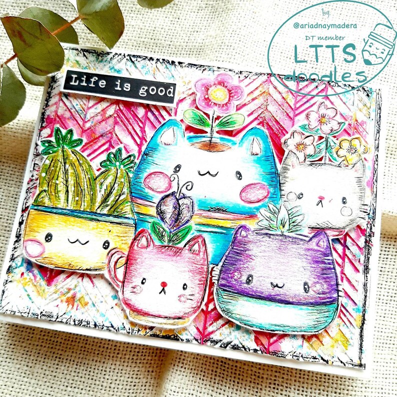 May include: A white card with a pink and white chevron pattern. The card has a black border and the text "Life is good" in black. There are five cartoon cats in flower pots, each with a different color and design. The cats are all smiling and have big eyes.