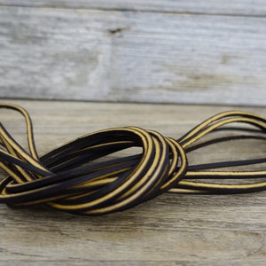 May include: A close-up of a bundle of black leather cord with a yellow stripe running along the edge. The cord is coiled and twisted together.
