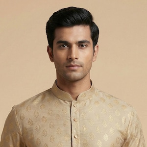 May include: A beige kurta with a mandarin collar and long sleeves. The fabric features a subtle, repeating gold pattern. The kurta has a button-down front and a pocket on the left side. The garment is worn by a person.