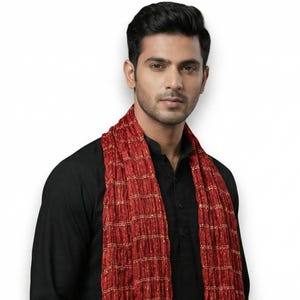 May include: A red and gold scarf with a textured, grid-like pattern. The scarf has gold stripes and tassels at the ends. The scarf is draped over a black outfit.