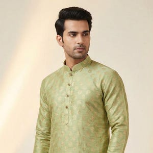 Può includere: Un kurta verde chiaro con colletto alla coreana e motivo floreale dorato. La tunica a maniche lunghe è abbinata a pantaloni color oro. L'outfit è in stile tradizionale indiano.