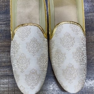 May include: A pair of white slip-on shoes with a gold trim and a white and gold patterned design. D. No. 1001