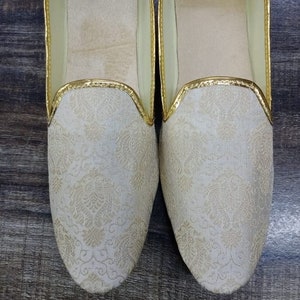 May include: A pair of white embroidered slippers with gold trim. The slippers have a pointed toe and a flat sole. D.No. 1005
