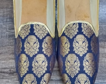 May include: A pair of black and gold patterned slippers with a pointed toe and a slip-on design.