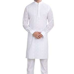 May include: A white long-sleeved kurta with intricate embroidery, worn by a person with short dark hair. The kurta has a mandarin collar and a button closure. The person is wearing white pants and brown shoes.