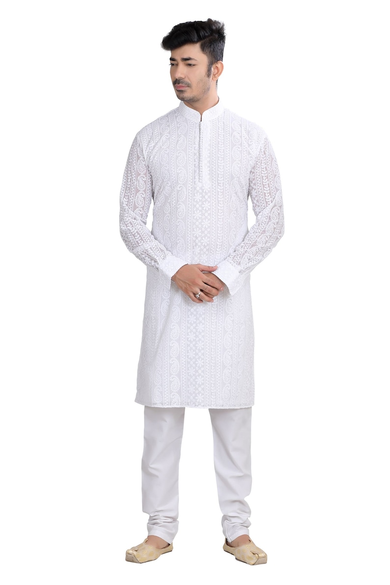 May include: A white long-sleeved kurta with intricate embroidery, worn by a person with short dark hair. The kurta has a mandarin collar and a button closure. The person is wearing white pants and brown shoes.
