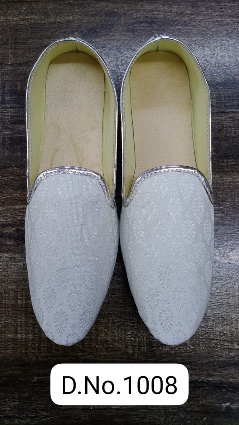May include: A pair of white, silver-trimmed, flat shoes with a floral pattern. The shoes have a pointed toe and a slip-on design. D.No.1008