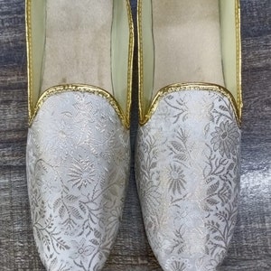 May include: A pair of white embroidered slippers with gold trim. The slippers have a floral pattern and are labeled "D.No.1007".