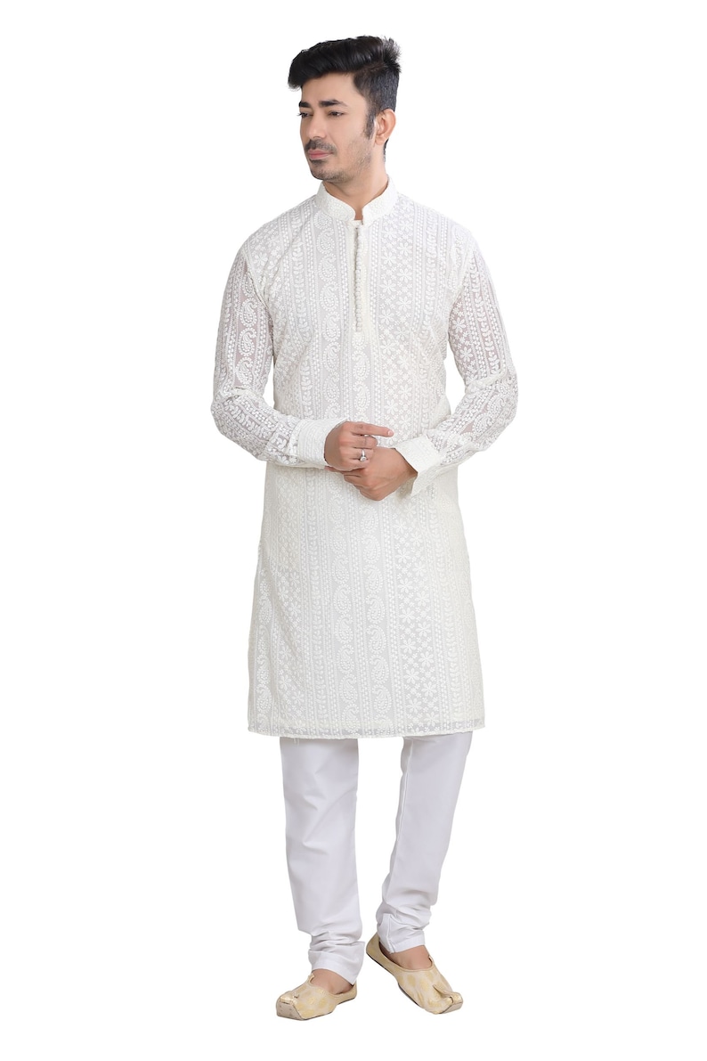 May include: A white long-sleeved kurta with intricate embroidery. The kurta has a mandarin collar and a button closure. The model is wearing white pants and beige shoes.
