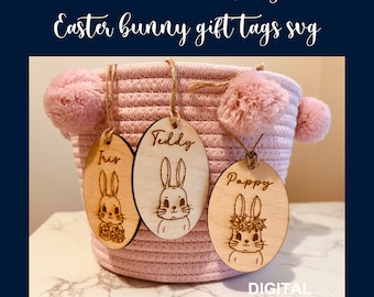 Pode incluir: Três etiquetas de presente de madeira em forma de coelho da Páscoa com os nomes Teddy, Iris e Poppy gravados nelas. As etiquetas estão penduradas em uma cesta rosa com pompons.
