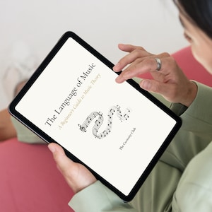 以下が含まれることがあります： 「The Language of Music, A Beginner's Guide to Music Theory」というタイトルの文書を表示するデジタルタブレット。画面には黒いテキストとS字型に曲がった五線譜のグラフィックが表示されており、その下に「The Curiosity Club」と印刷されています。