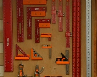 May include: A collection of red and orange woodworking tools, including rulers, squares, and a compass, are displayed on a wooden board. The tools are arranged in rows and columns, and some of them have labels with numbers on them.