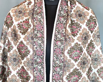 May include: A white shawl with a floral pattern in shades of brown, pink, and green. The shawl has a decorative border with a repeating floral design.