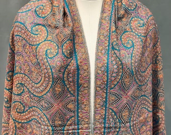 May include: A paisley patterned shawl in teal, brown, and pink hues, draped over a mannequin. The intricate design features swirling floral motifs and a border with vertical stripes. The shawl is made of a soft, flowing fabric.