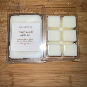 May include: Two clear plastic clamshell containers holding white wax melts. One container holds a large rectangular melt, the other holds six square melts. The label reads "Blaze & Bubbles Honeysuckle Jasmine Soy Blend Wax Melts Net Wt 2.5 oz (70.9g)".