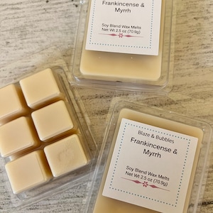 May include: Three clear plastic containers of soy blend wax melts. The labels read "Blaze & Bubbles Frankincense & Myrrh" and "Net Wt 2.5 oz (70.9g)." One container holds six individual wax melt cubes. The wax is a light beige color.