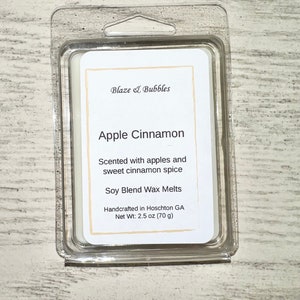 May include: A clear plastic package containing soy blend wax melts. The label reads "Apple Cinnamon" and "Scented with apples and sweet cinnamon spice." The net weight is 2.5 oz (70 g). The brand name is "Blaze & Bubbles."