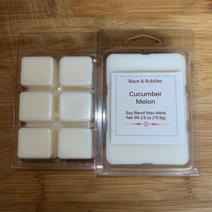 May include: Two clear plastic clamshells containing off-white soy blend wax melts. One package has six square melts, the other has a solid block. The label reads "Blaze & Bubbles Cucumber Melon Soy Blend Wax Melts Net Wt 2.5 oz (70.9g)."