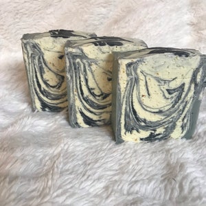 May include: Three handmade soap bars with a marbled design. The soap features swirls of black and gray against a creamy white base. The bars are rectangular and appear to be freshly cut.