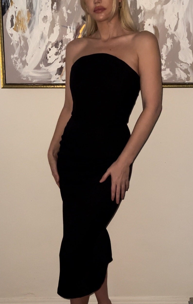 May include: A black strapless midi dress with a fitted bodice and a slightly flared skirt.