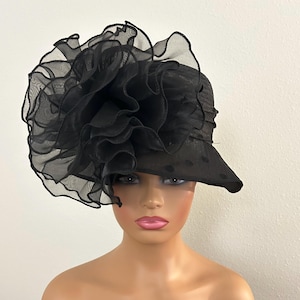 May include: A black hat with a wide brim and a large, ruffled flower detail. The hat is made of a sheer, possibly organza-like material, with a polka dot pattern on the brim. The hat is designed for formal occasions.