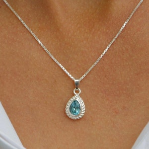 May include: A silver chain necklace with a teardrop-shaped pendant featuring a light blue gemstone.