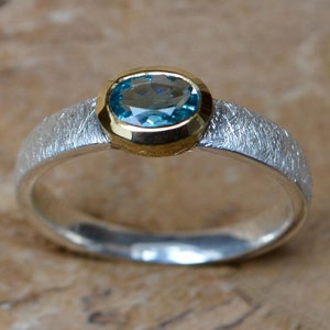 May include: A silver ring with a textured band and a blue gemstone set in a gold bezel.