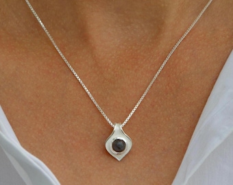 May include: A silver chain necklace with a pendant featuring a dark gray stone set in a silver teardrop-shaped design.