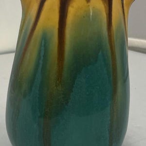 May include: A teal ceramic vase with brown and yellow glaze. The vase has a rounded body and two small handles on the top.
