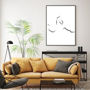Puede incluir: Una impresi&oacute;n de arte en l&iacute;nea negra y blanca de una pareja abraz&aacute;ndose, enmarcada en un marco negro y colgada en una pared blanca sobre un sof&aacute; amarillo con almohadas negras.
