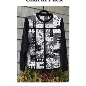 May include: A black and white quilted sweatshirt jacket with a floral patchwork design. The jacket has long black sleeves and a black zipper. The text "Charm Pack" is at the top, and "Quilted Sweatshirt Jacket" is at the bottom.