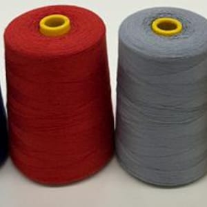 May include: Four spools of thread in a row, each with a yellow core. The colors are blue, red, gray, and yellow. The thread is tightly wound around the spools, creating a conical shape. The spools are on a white surface.