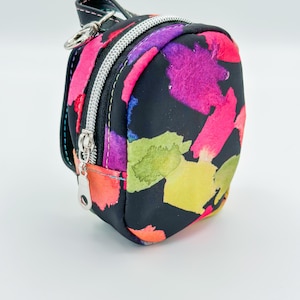 May include: A small black backpack with a colorful watercolor print. The backpack has two zippered compartments and a silver zipper pull.