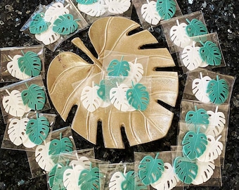 May include: A collection of green and white leaf-shaped decorations, some with a textured surface, arranged on a gold-colored surface. The decorations are in various sizes and shapes, and some have a raised design.