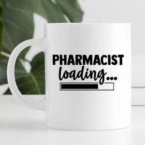 May include: White ceramic mug with a black handle. The mug features the text "PHARMACIST loading..." in black, with a loading bar graphic below. The mug is likely a gift for a pharmacist.