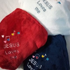 May include: Three fleece blankets with the words "JESUS Loves me" embroidered on them. The blankets are red, white, and blue. Each blanket has a musical note and heart design.