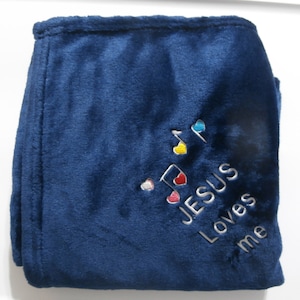 May include: A navy blue plush blanket with embroidered text and musical notes. The text reads "JESUS Loves me" in white thread. The musical notes are decorated with colorful hearts.