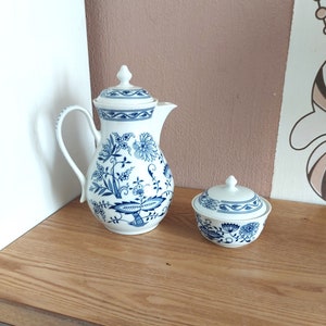 May include: A white porcelain teapot and sugar bowl with a blue and white floral pattern. The teapot has a handle and a lid. The sugar bowl has a lid.
