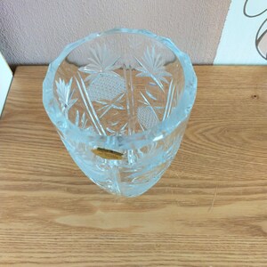 May include: A clear glass vase with a cut-glass design. The vase has a round base and a tall, slender body. The vase is decorated with a geometric pattern.