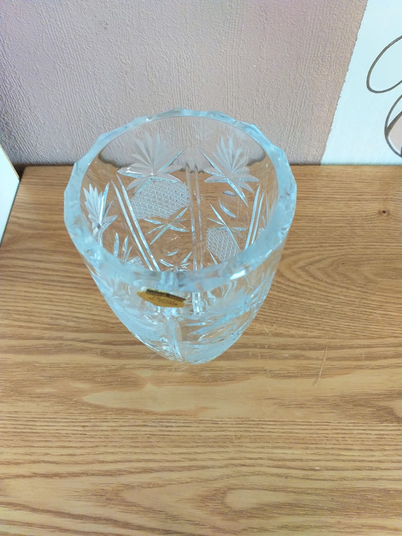 May include: A clear glass vase with a cut-glass design. The vase has a round base and a tall, slender body. The vase is decorated with a geometric pattern.