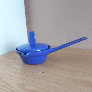 May include: A blue ceramic gravy boat with a lid and a handle. The boat has a spout for pouring.