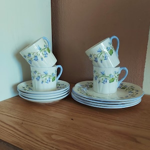 Peut inclure: Service à thé vintage composé de tasses et de soucoupes blanches ornées de motifs floraux bleus et de poignées et bords bleu clair. L'ensemble comprend quatre tasses et soucoupes, disposées sur une surface en bois.