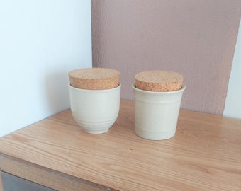 May include: Two ceramic jars with cork lids. The jars are a light beige colour and have a slightly textured surface. The lids are a natural cork colour.