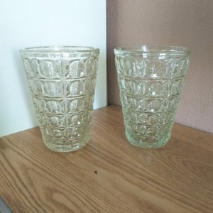 Könnte beinhalten: Zwei klare Glasvasen mit einem strukturierten, geometrischen Muster. Die Vasen stehen auf einer Holzoberfläche.