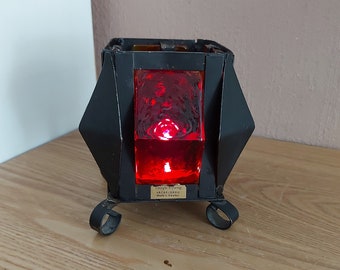 Puede incluir: Candelero de metal negro con un inserto de vidrio rojo. El candelabro tiene una base cuadrada con cuatro patas y una etiqueta que dice "Design: Yvonne Jackelsand Made in Sweden".