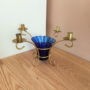 Könnte beinhalten: Ein Vintage-Kerzenhalter mit einer tiefblauen Glasschale und vier Kerzenhaltern. Die Kerzenhalter sind aus goldfarbenem Metall gefertigt und haben ein geschwungenes Design. Die Schale hat einen gerüschten Rand.