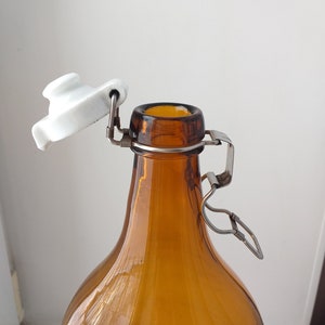 May include: A brown glass bottle with a white ceramic swing top lid. The bottle has a metal wire closure.