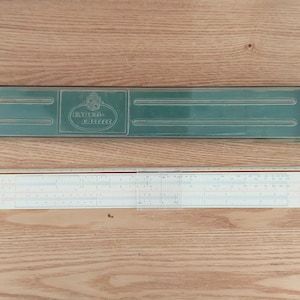 May include: A vintage slide rule with a green plastic case. The case has the text "Faber Castell" printed on it. The slide rule is made of white plastic and has a black and white scale.