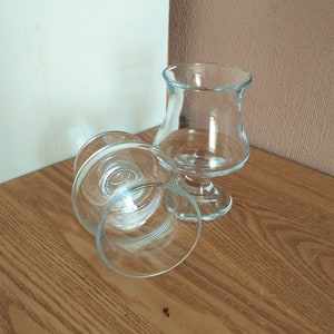 Puede incluir: Dos copas de vidrio transparente con base de tallo. Las copas están sobre una superficie de madera.